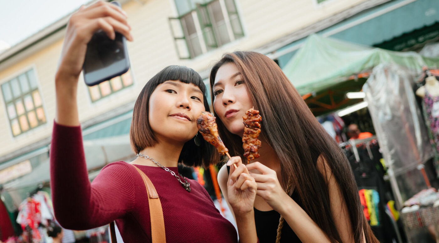 Tourists selfie with Moo Ping or Grilled Pork Skewers, Thai street food (Photo Credit: iStockphoto)