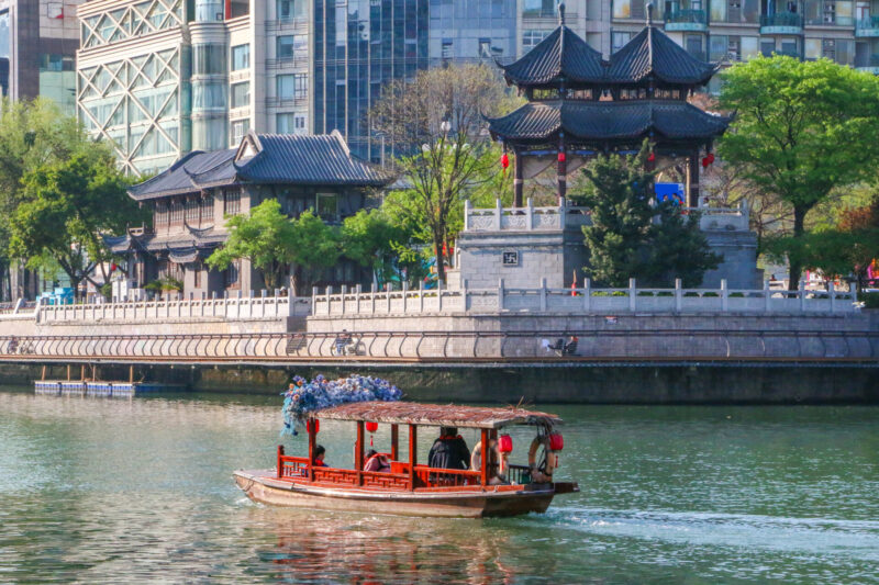 A wooden Chinese boat on the Jinjiang river about to head pass the Hejiang Pavilion.