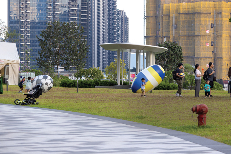 Families enjoy open green spaces with the harbor as backdrop, exemplifying Kai Tak&rsquo;s vision as a neighborhood for leisure and play.