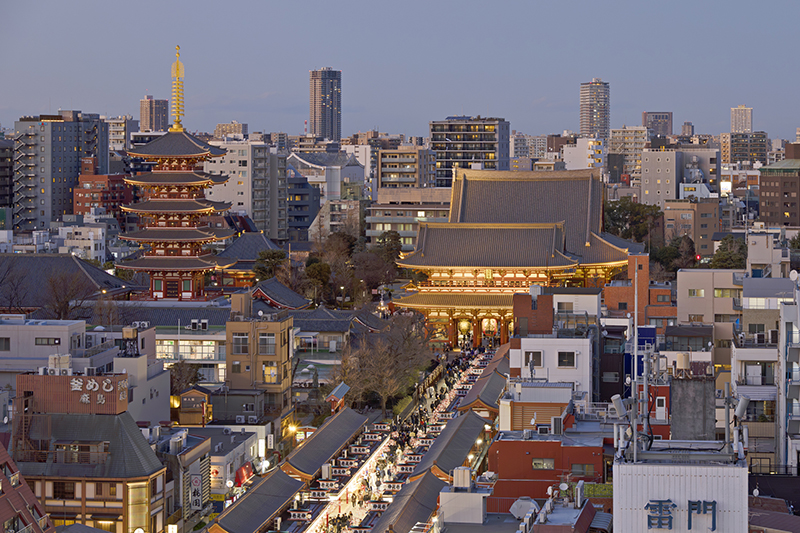 Senso-ji Temple and its pagoda in the Asakusa district of Tokyo, illuminated at dusk with the surrounding city skyline.