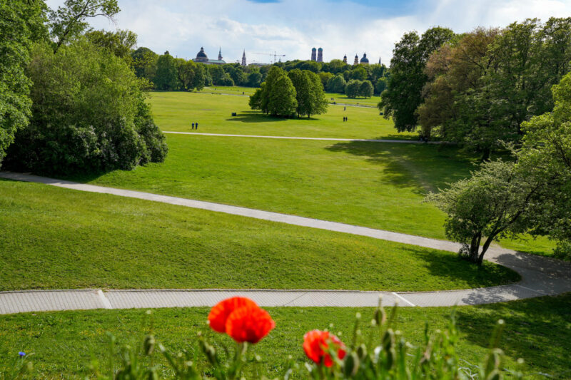 Vast green English Garden showing Munich skyline with Frauenkirche towers.